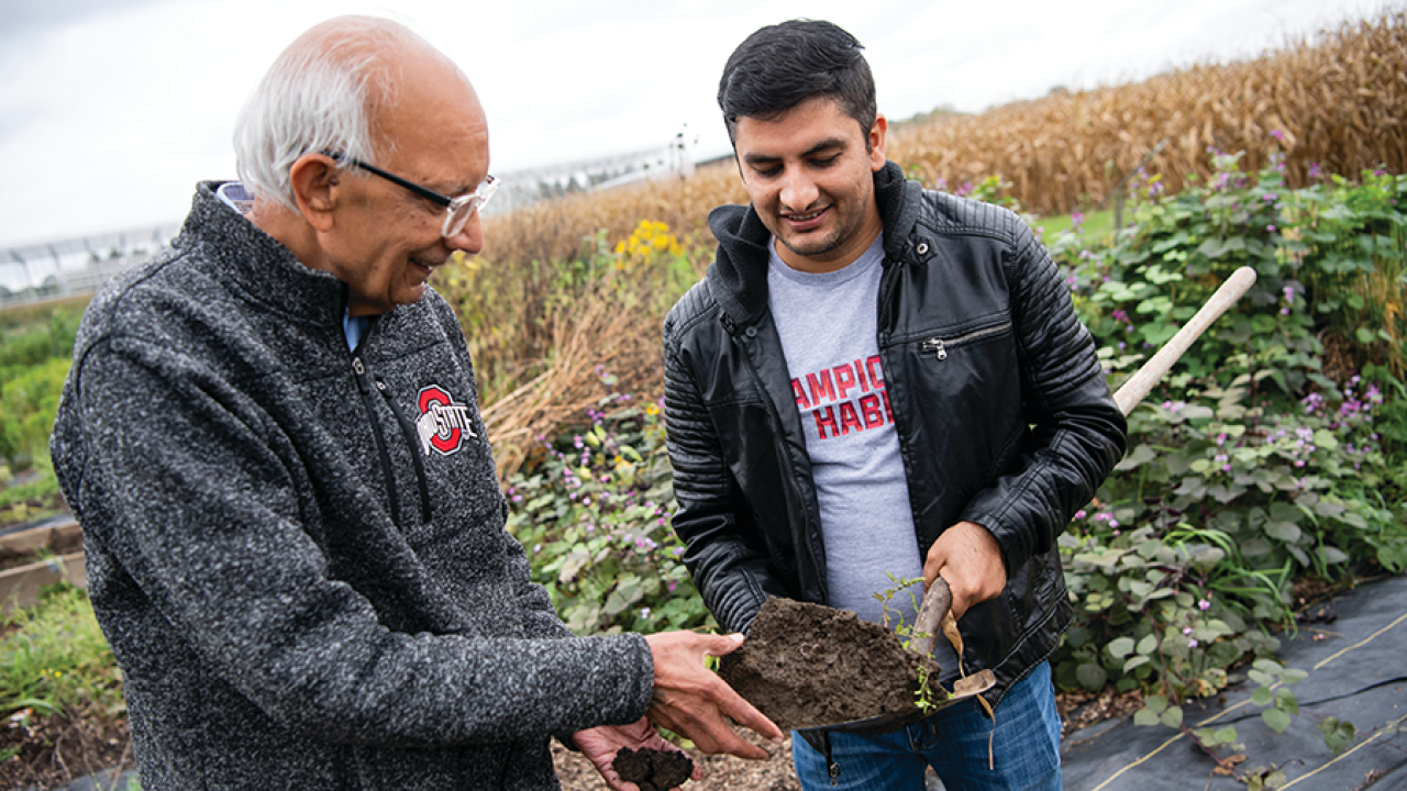 Two individuals outdoors in a field reviewing the soil on a shovel.